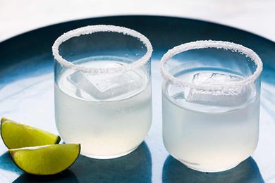 Two classic margaritas in glasses with salted rims and lime wedges off to the side
