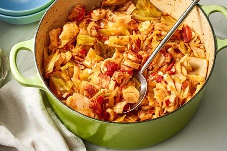 Angled view of a green dutch oven of swamp cabbage with a metal serving spoon