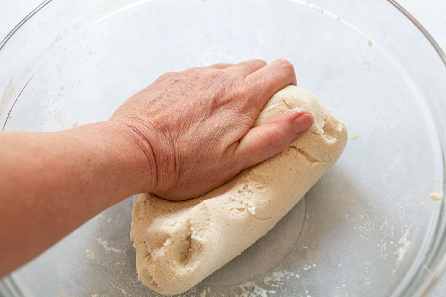 A hand kneading dough in a glass bowl