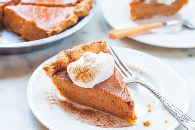 Slice of sweet potato pie on a white plate with whipped cream dusted with cinnamon and fork.