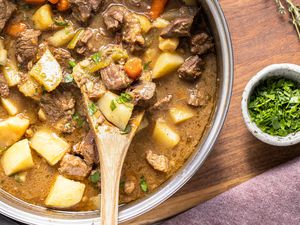 Pot of Easy Beef Stew with a Wooden Spatula, a Small Bowl of Parsley, a Sprig of Thyme, and a Kitchen Towel