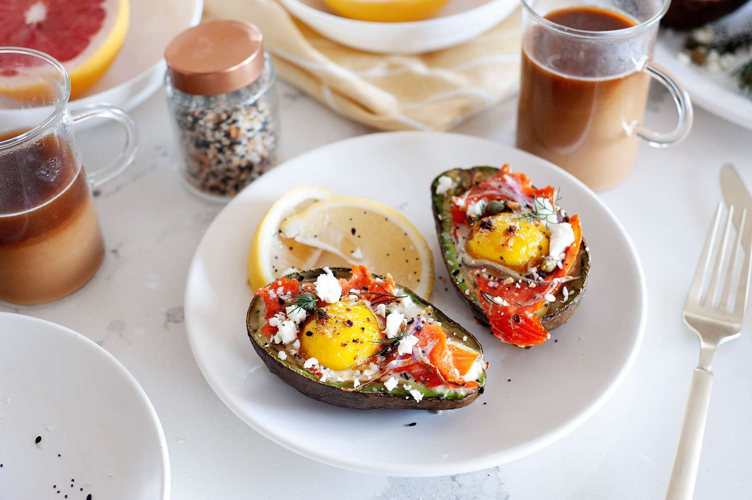 Baked eggs in an avocado on a plate with a lemon. Sliced grapefruit and coffee are behind it.