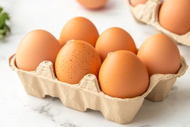 Six eggs in a cardboard carton, on a marble surface with another carton partially visible in the background