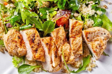 Sliced grilled chicken breast on a bed of greens and quinoa salad