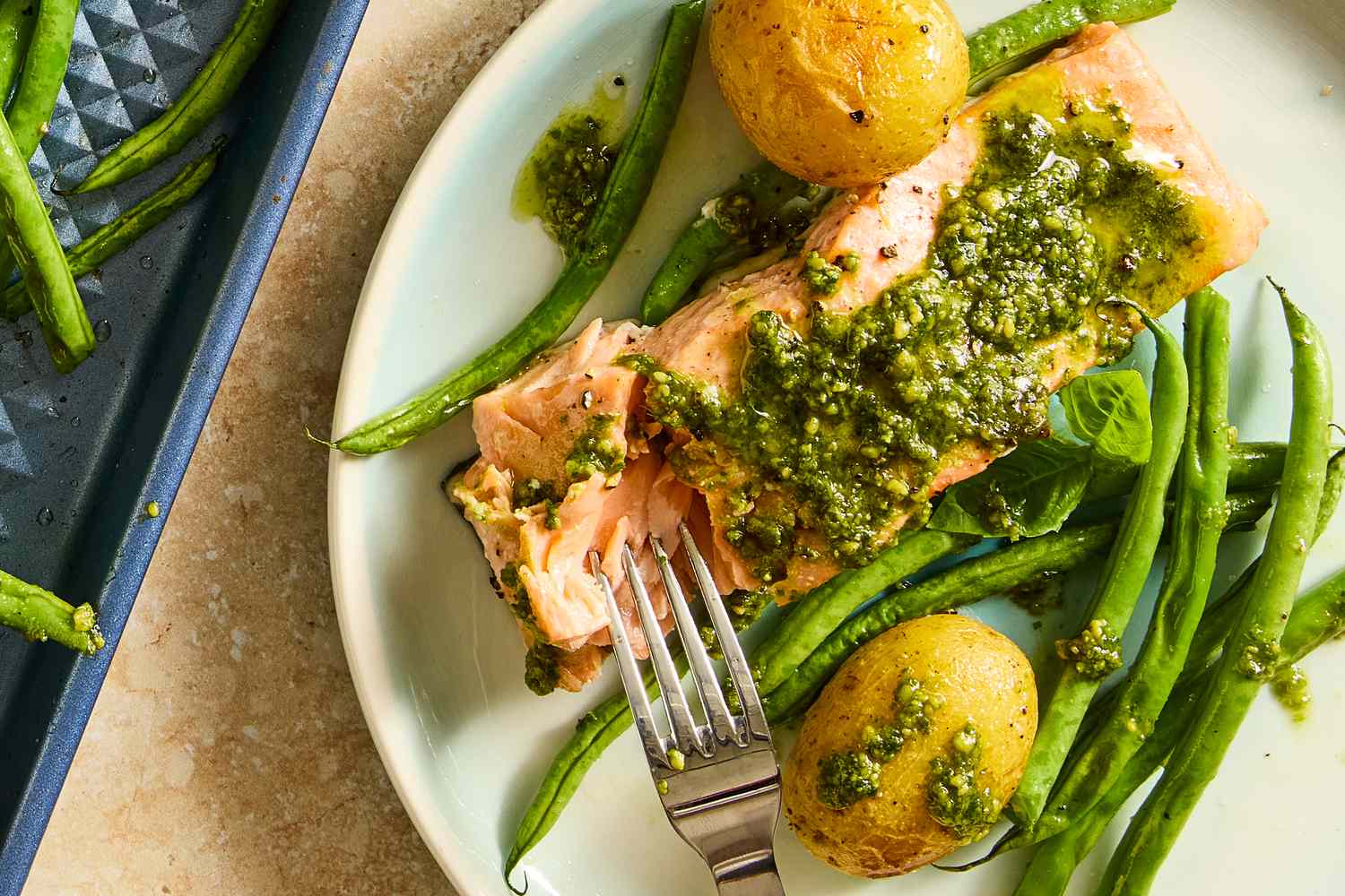 A plate with a fork cutting into a piece of salmon from the salmon with potatoes and pesto recipe