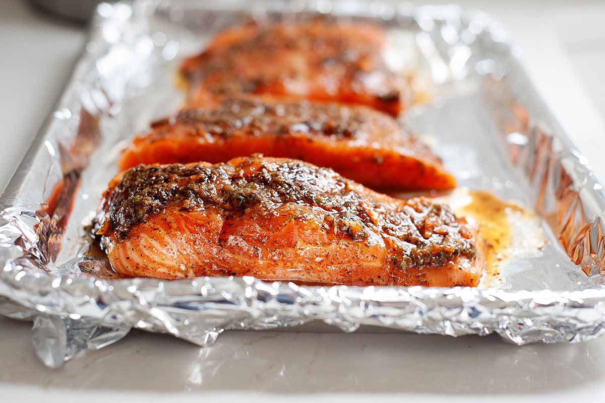 Side view of jerk salmon on a foil-lined baking tray. Seasoning coats the top of the salmon.