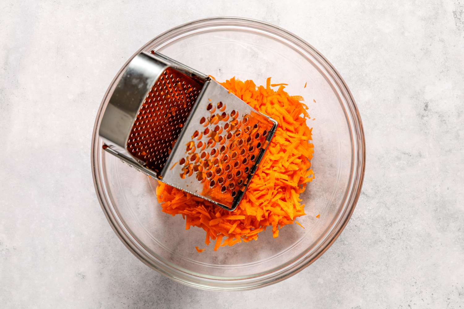 Shredded carrots in a glass bowl with a box grater for Easy Carrot Cake recipe