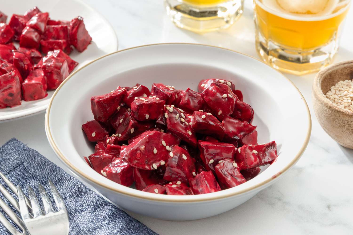 Side view of a bowl with chopped pieces of beets in a creamy sauce, topped with sesame seeds