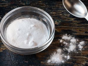 A small glass bowl of baking powder with a measuring spoon on a wood surface