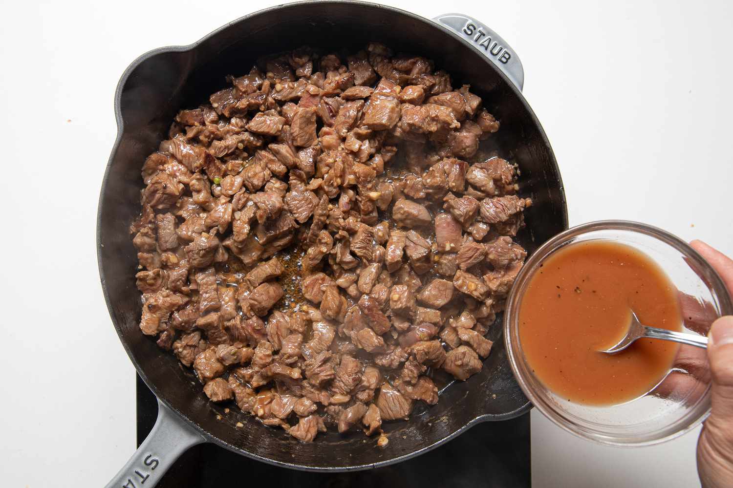 Bowl of Sauce Poured Over Beef Cooking in a Cast Iron Skillet for Cambodian Shaking Beef Recipe