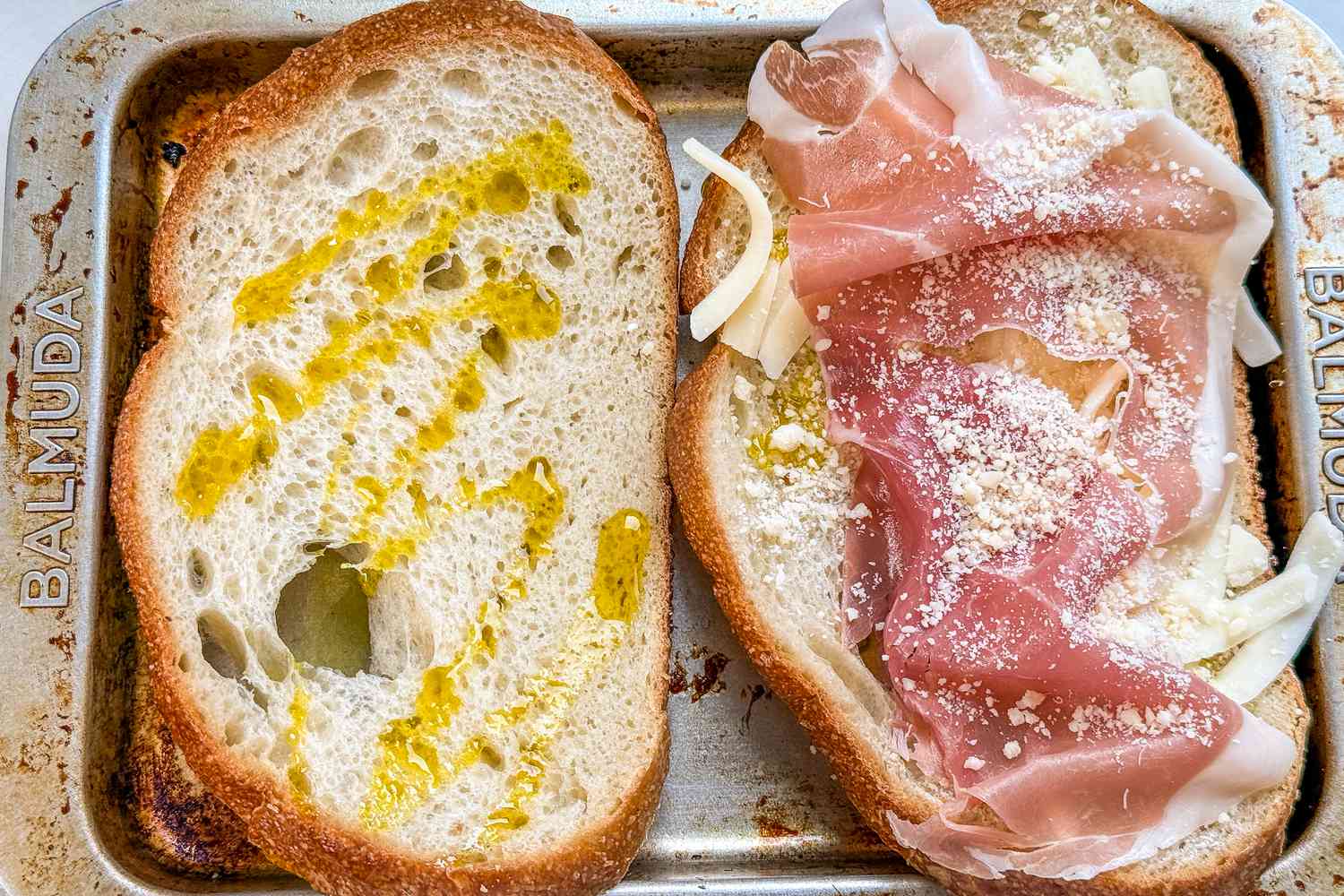 Overhead view of two untoasted pieces of ham and cheese toast one with just the oil added on a toaster oven tray