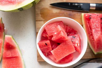 A bowl of cut watermelon over a cutting board with pieces of cut watermelon and a paring knife