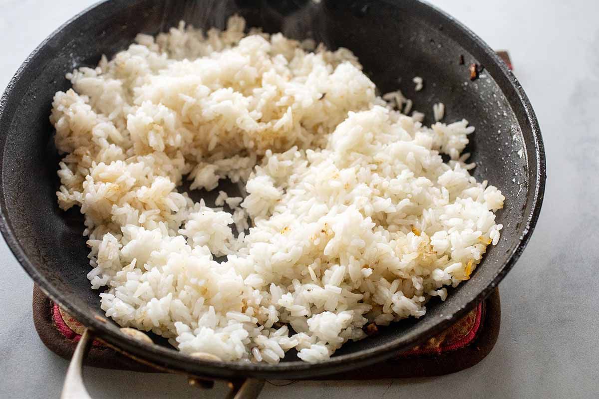 Black skillet set on a potholder. The skillet has cooked white rice inside for fried rice recipe.