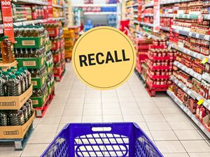 Looking down a grocery store aisle from behind a shopping cart. A "Recall" badge is superimposed over the center of the image.