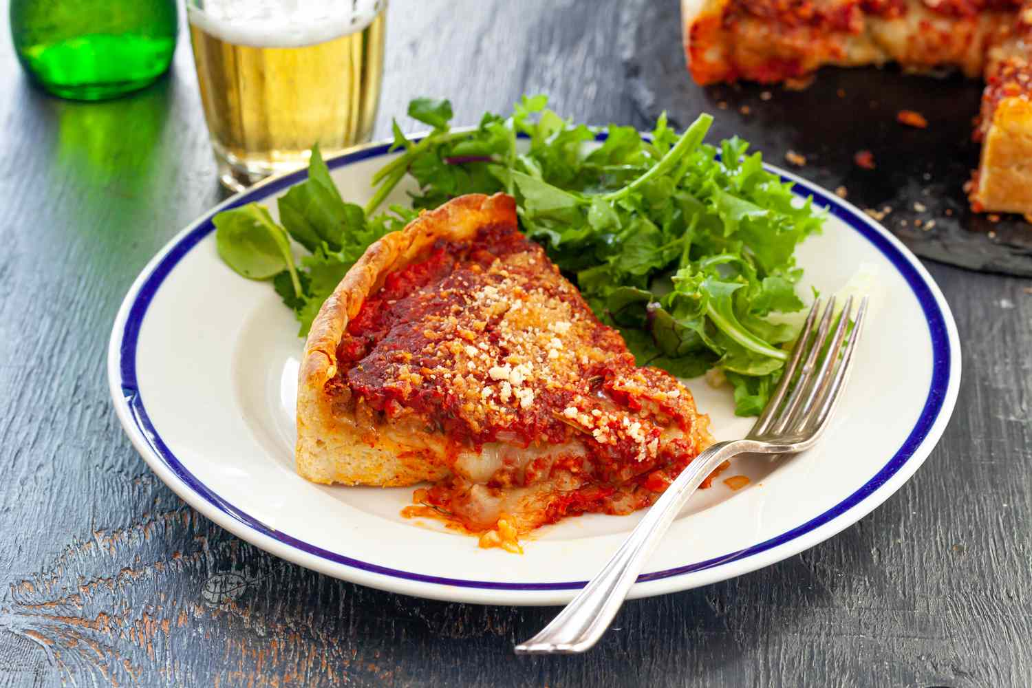 A slice of Italian Sausage Deep Dish Pizza on a plate with a salad.