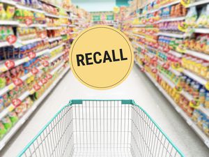 A shopping cart in a supermarket aisle, a circular sign with the word 'Recall' displayed prominently in the center