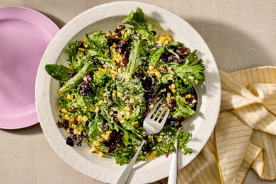 A plate of corn and black bean salad with leafy greens, garnished and served with utensils
