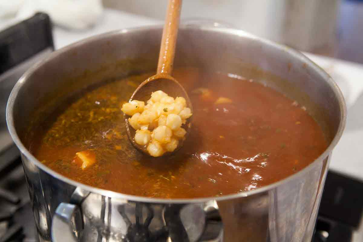 A wooden spoon with White Corn over Pozole Rojo 