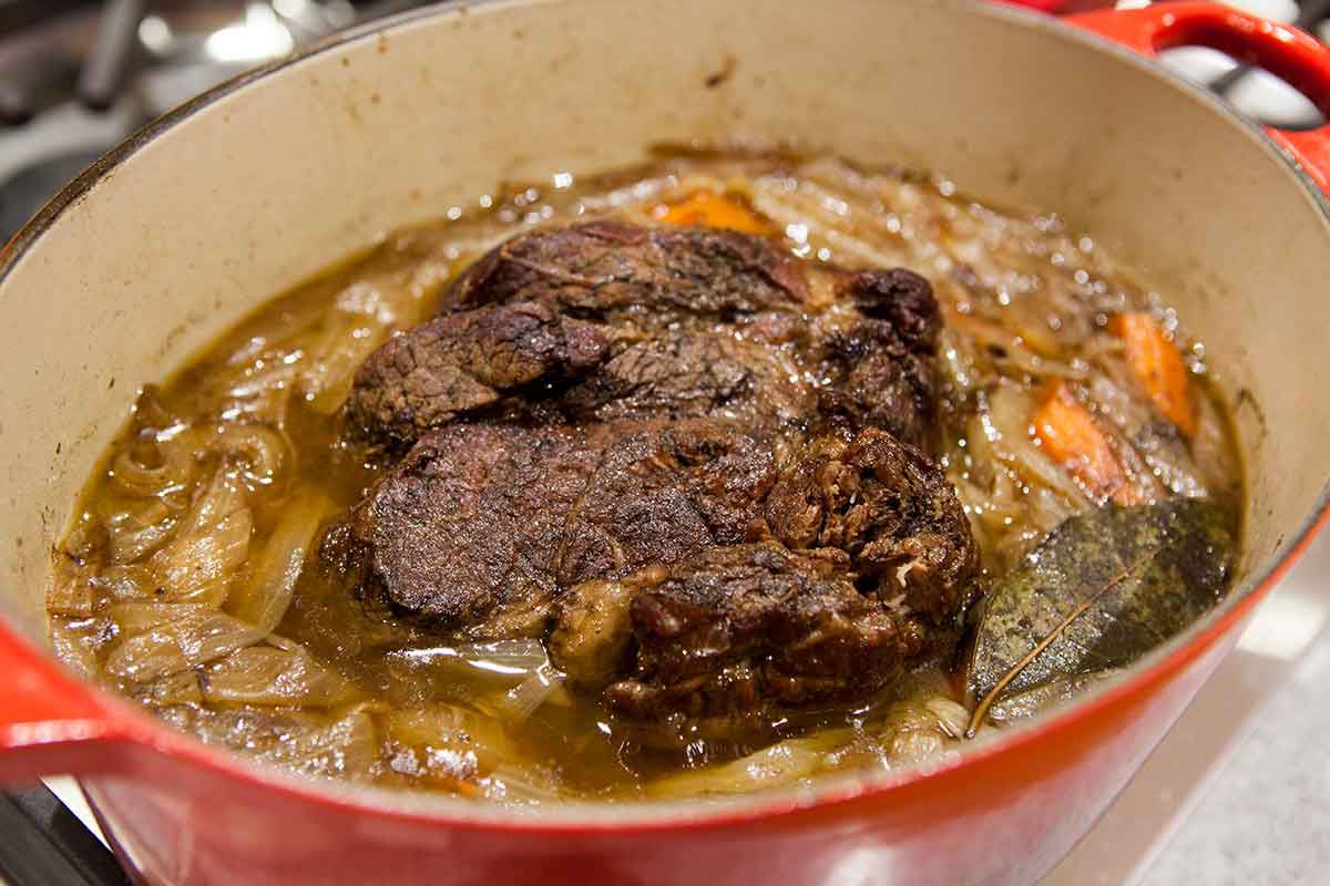 Pot roast beef simmering in pot on the stovetop in a liquid