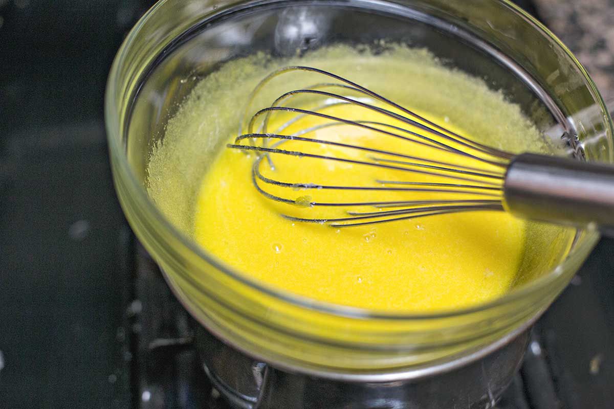 A glass bowl of whisked eggs and sugar over a pan of simmering water