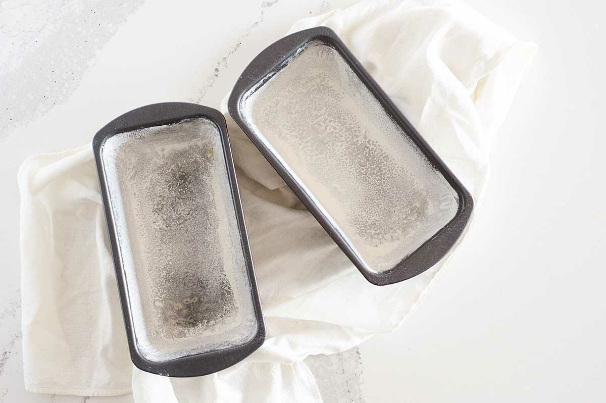 Two loaf pans lined with parchment paper and lightly floured to show how to make Vegan Pumpkin Bread.