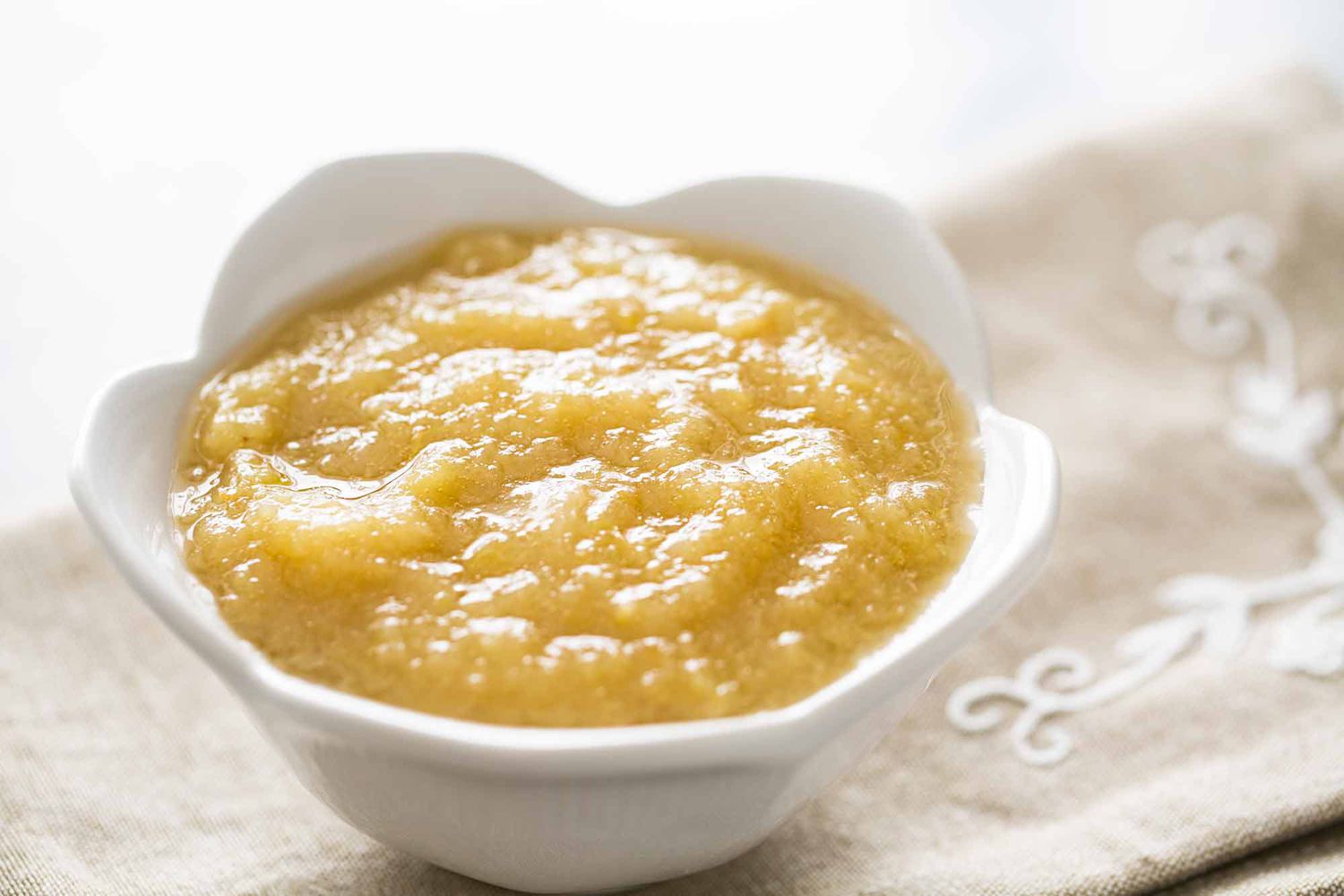 A bowl of homemade applesauce in a white bowl resting on a cloth napkin 
