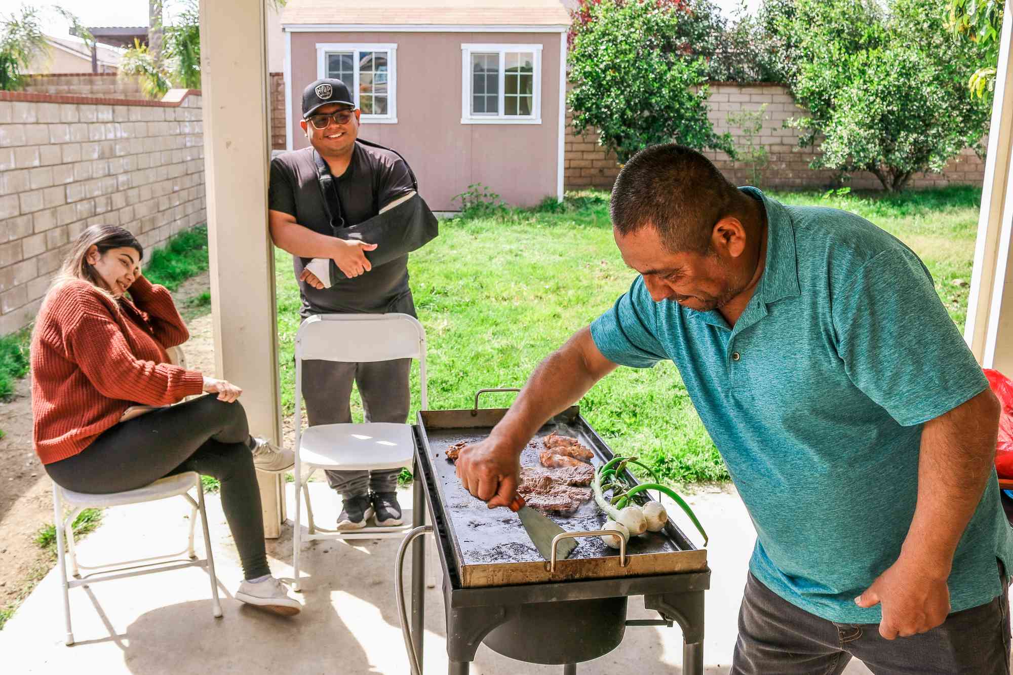 Mario Ayala grilling outside on the comal, with his adult children nearby