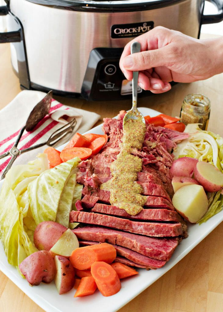 A hand drizzling mustard sauce over sliced corned beef