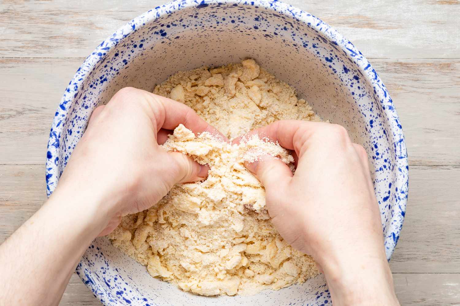 Hands working butter into dough to make a crumbly mixture