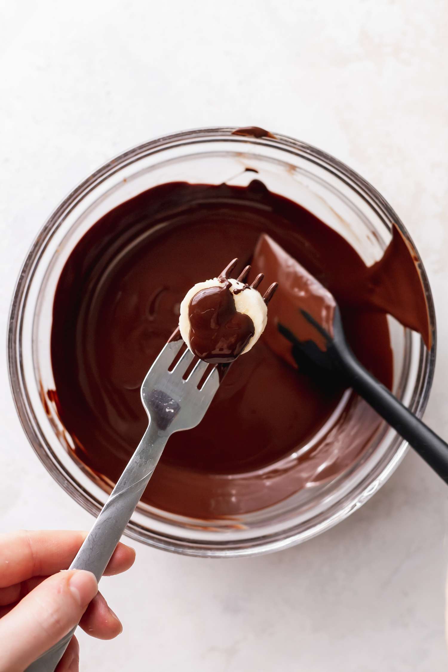 Melted Chocolate Chips in a bowl with a banana slice being dipped in