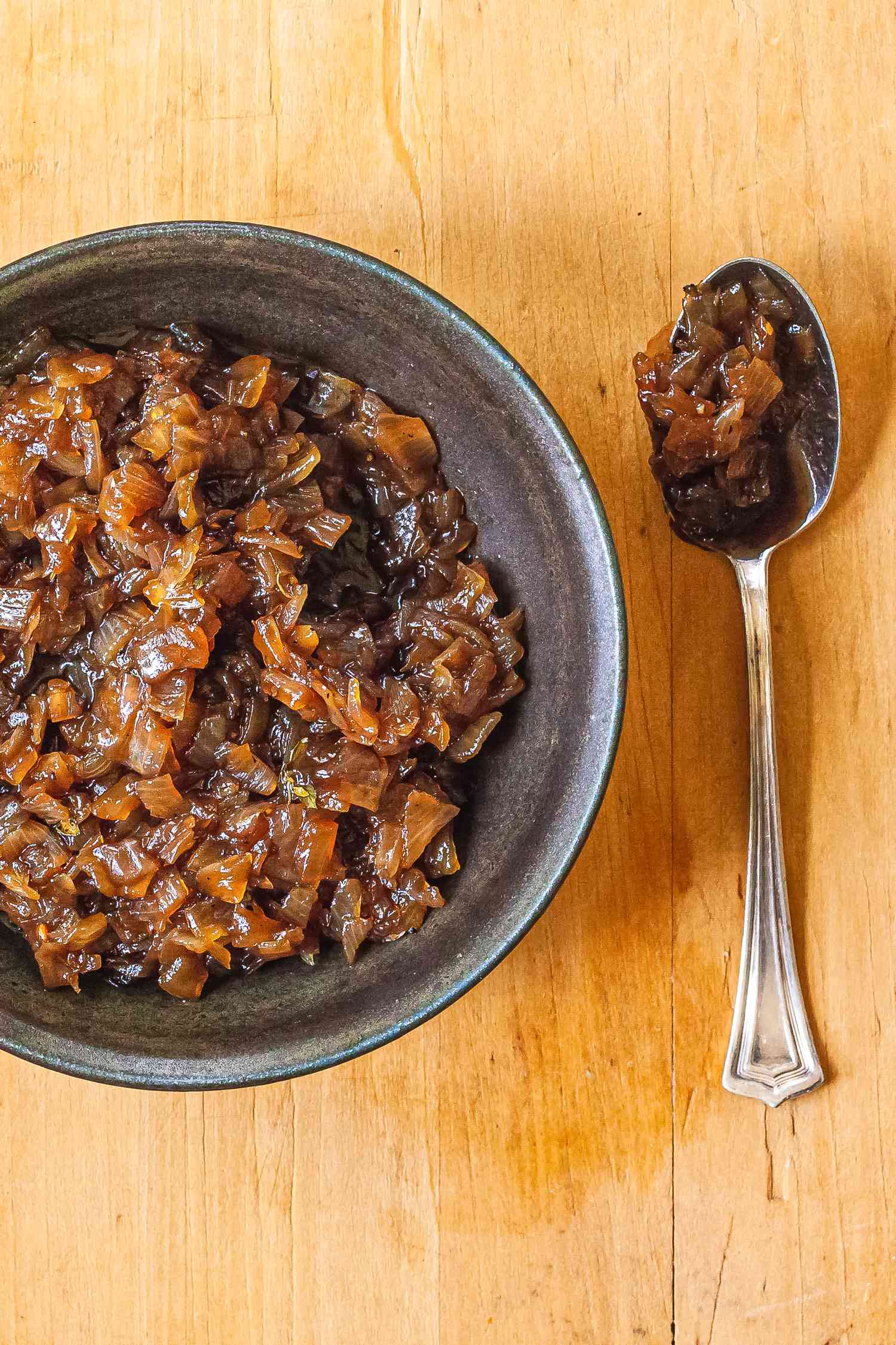 A grey bowl with balsamic onion jam and a spoon next to it.
