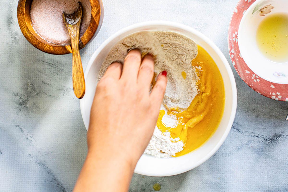 Woman's hand mixing Ingredients to make dough -- flour, slat and butter or ghee in three small bowls on a marble counter.