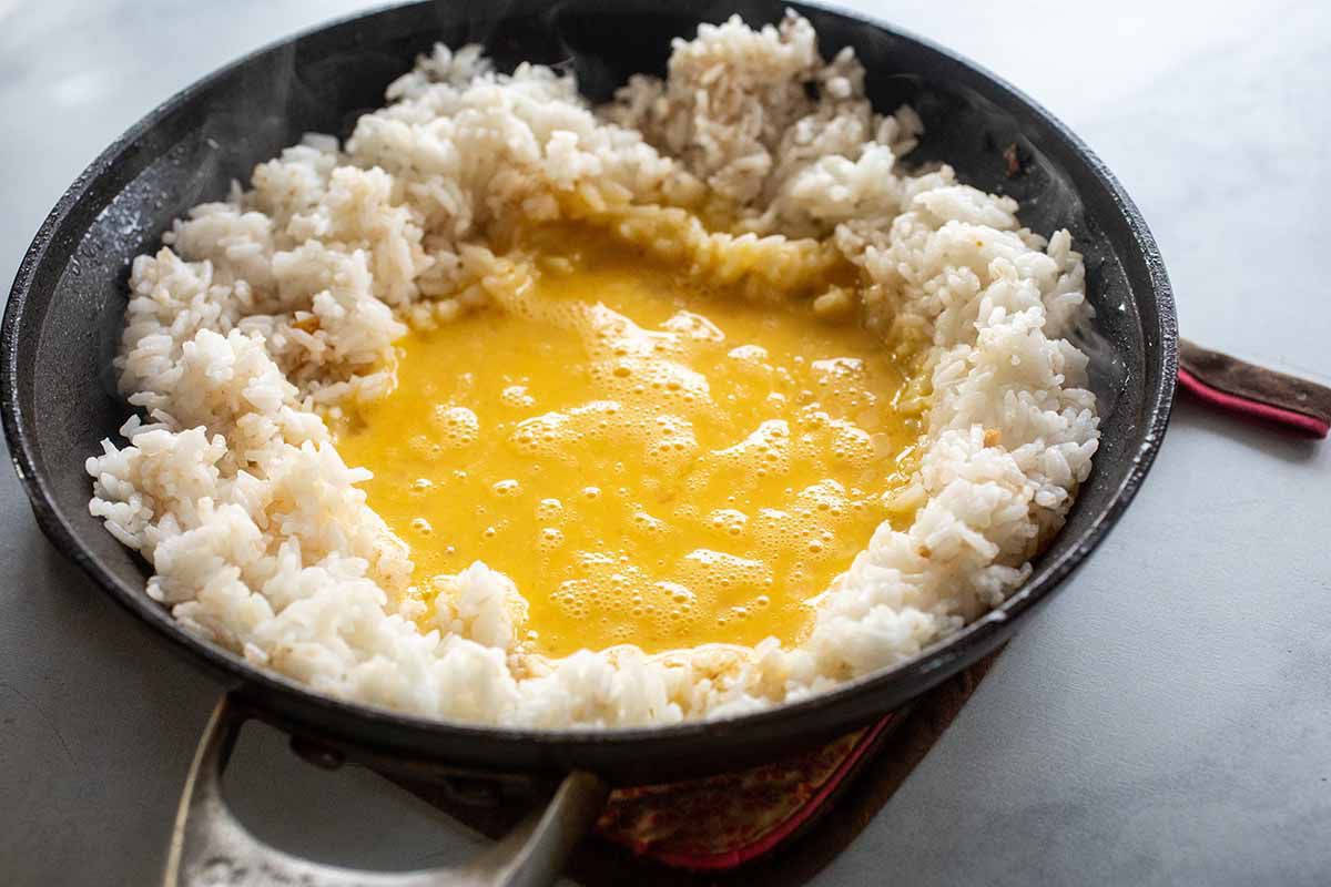 A black skillet with cooked white rice with a well of whisked eggs inside.