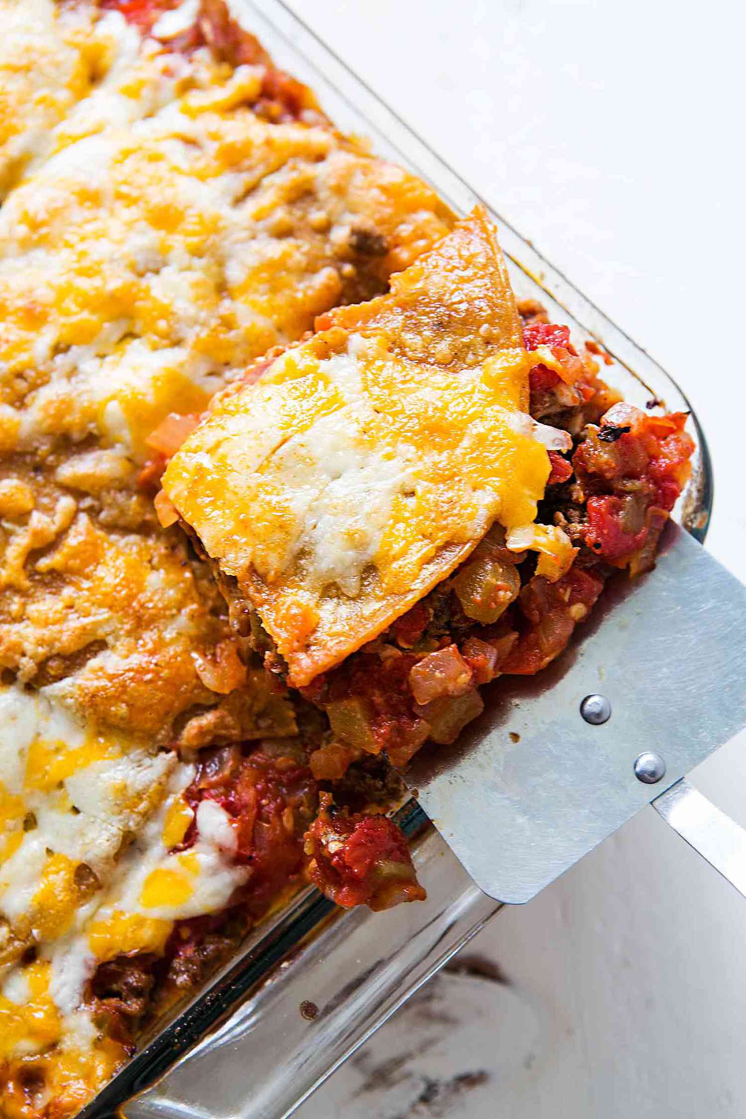 Sliced taco lasagna made with tortillas, beans, beef, tomatoes, and cheese in a baking dish